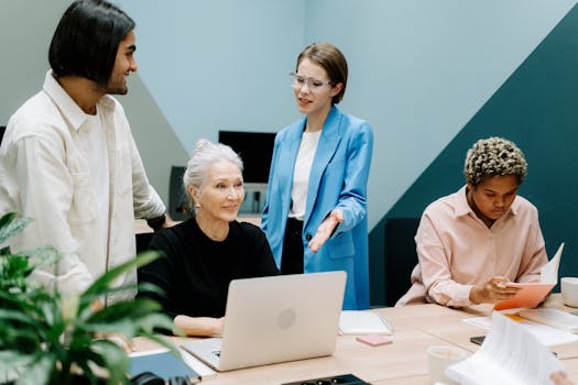 A group of professionals engaged in a collaborative meeting at an office with laptops and documents.