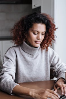 A woman working from home, typing on a laptop in a cozy setting, showcasing concentration and modern lifestyle.